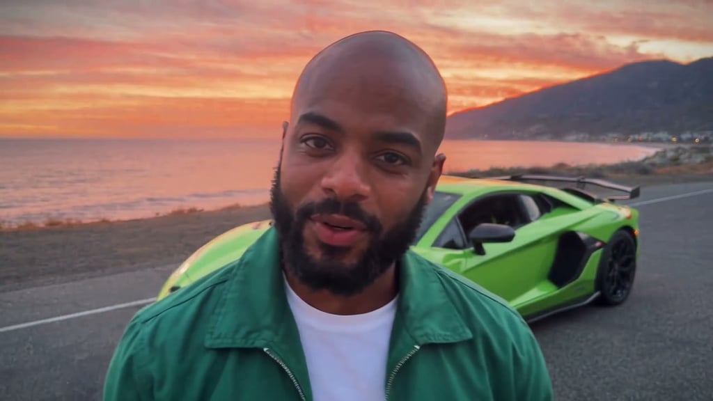 A man in a green jacket on a sunset coast road with a green Lamborghini Aventador parked behind him