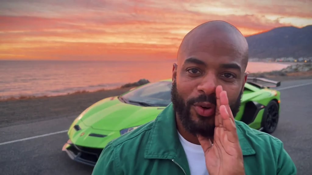 A man in a green jacket talks to the camera on a sunset coast road with a green Lamborghini Aventador parked behind him